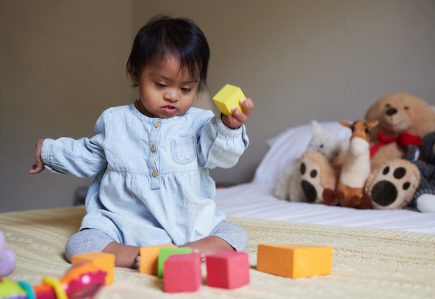 Kindertagesstätte mit Down-Syndrom und Baby auf dem Bett mit Spielzeug, das mit Farbformen und -blöcken spielt Besondere Bedürfnisse der Kinderentwicklung und süßes Mädchen im Schlafzimmer lernen Spaß und Therapiespiele für Kinder