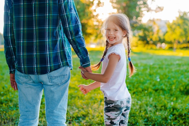 Kindertochter des kleinen Mädchens, welche die Hand ihres Vaters in der Natur bei Sonnenuntergang hält.