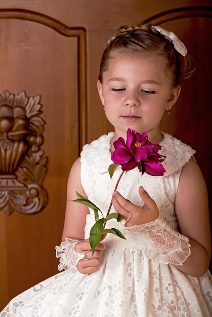Kinderurlaub Elegantes Mädchen in einem weißen Kleid Mädchen mit frischem Pfingstrosen-Bouquet auf Holzhintergrund
