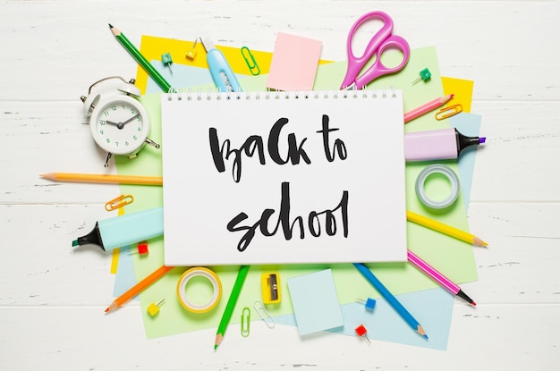 Kinderzubehör für Lernkreativität und Bürobedarf auf weißem Holzhintergrund Handschriftliche Aufschrift Zurück zur Schule auf einem weißen Notizbuch