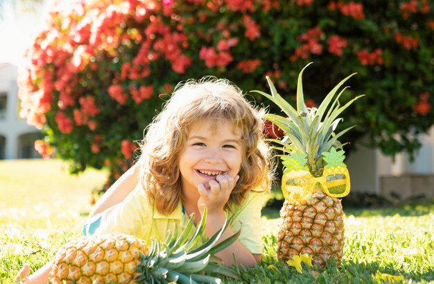 Kindesjunge hält eine Ananas, die Sommernatur Hintergrund mit Kopierraum gesunde Früchte für