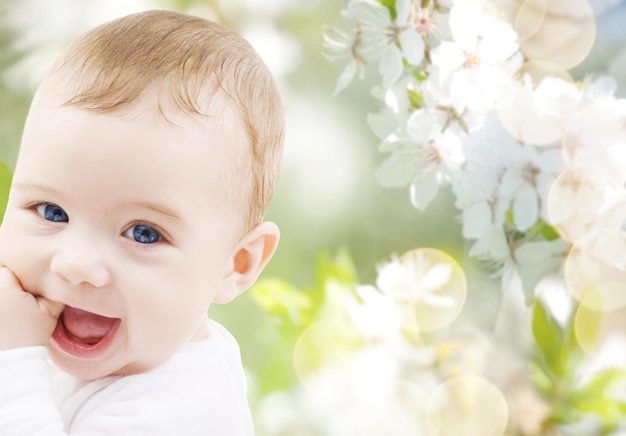 Kindheit, Babyalter, Sommer, Frühling und Gesundheitskonzept - Nahaufnahme eines glücklichen Jungen oder Mädchens über grün blühendem Gartenhintergrund