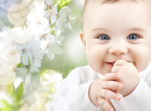 Kindheit, Babyalter, Sommer, Frühling und Gesundheitskonzept - Nahaufnahme eines glücklichen Jungen oder Mädchens über grün blühendem Gartenhintergrund