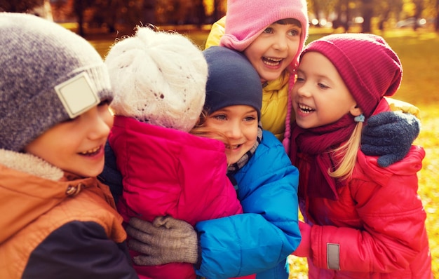 Foto kindheit, freizeit, freundschaft und menschenkonzept - gruppe glücklicher kinder, die sich im herbstpark umarmen