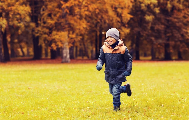 kindheit, freizeit und personenkonzept - glücklicher kleiner junge, der auf herbstparkfeld läuft