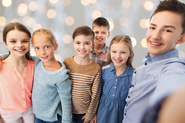 Foto kindheit, freundschaft, technologie und personenkonzept - glückliche kinder, die selfie über feiertage sprechen, beleuchten hintergrund