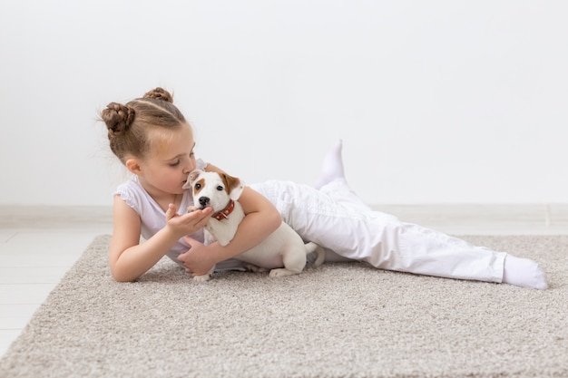 Kindheit, Haustiere und Hundekonzept - Kleines Kindermädchen, das mit Welpen auf dem Boden posiert.