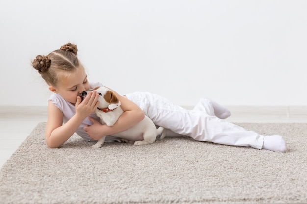 Kindheit, Haustiere und Hundekonzept - Kleines Kindermädchen, das mit Welpen auf dem Boden posiert.