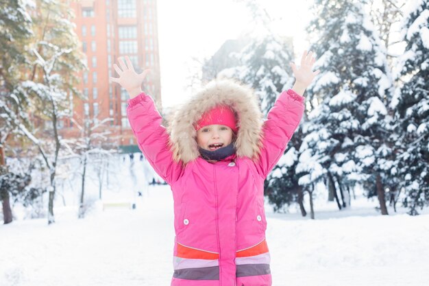 Kindheit, Mode, Jahreszeit und Menschenkonzept - 4K Little Girl Playing in Snow Winter, View Happy Child Making Snowball, Snowman Par, Kids in Christmas Vacation. Gesicht eines glücklichen Mädchens in Winterkleidung