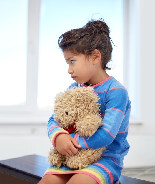 Kindheit, traurigkeit, einsamkeit und menschenkonzept - trauriges kleines mädchen mit teddybärspielzeug zu hause
