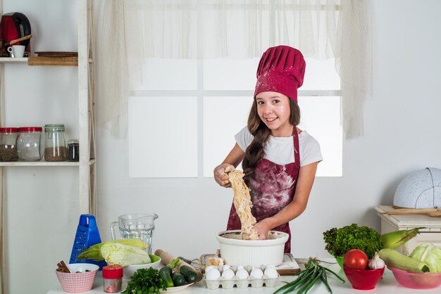 Kindheitsentwicklung kleines Mädchen, das in der Küche backt, Kind, Koch, Kochen, Teig machen, Kind, bereitet gesundes Essen zu Hause zu und trägt Koch, einheitliche Haushaltsführung und Haushaltshilfe, Kalorien und Ernährung