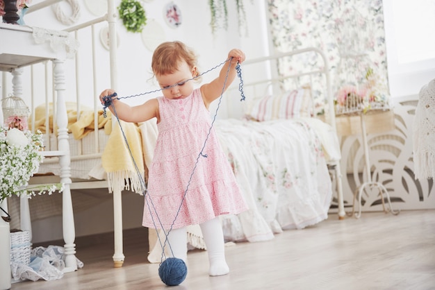 Kindheitskonzept. Baby im netten Kleiderspiel mit farbigem Thread. Weißes Vintage Kinderzimmer