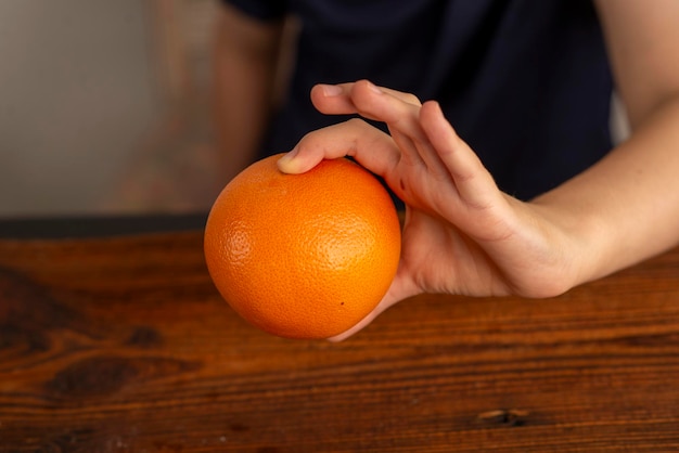 kindische Hände, die eine Orange über den Tisch halten