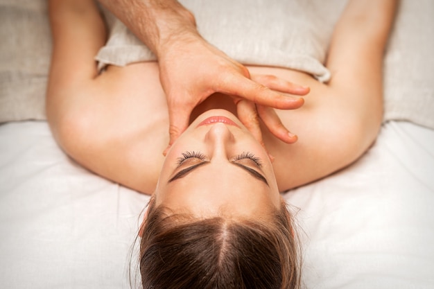Kinn- oder Nackenmassage einer jungen Frau durch die Hand eines männlichen Massagetherapeuten in einem Spa-Salon