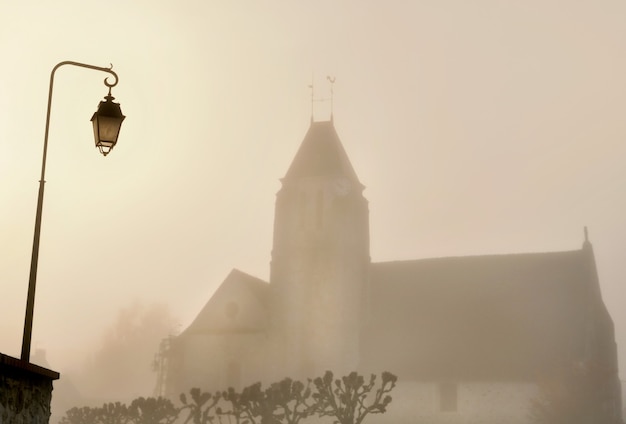 Kirche eines ländlichen französischen Dorfes und eines Laternenpfahls im Nebel