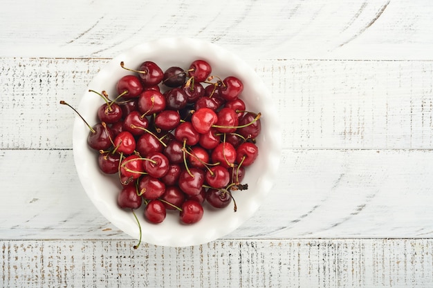 Kirsche mit Wassertropfen auf weißer Schüssel auf weißem Steintisch. Frische reife Kirschen. Süße rote Kirschen. Ansicht von oben. Rustikaler Stil. Obst Hintergrund