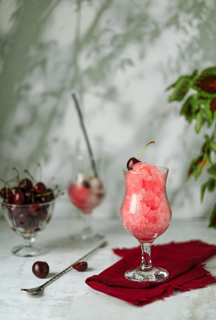 Kirschgranita, Beeren in einer Glasvase und erfrischendes Getränk mit Eis auf hellgrauem Hintergrund