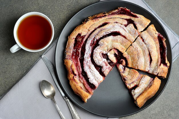 Kirschkuchen auf einem schwarzen Teller und eine Tasse Tee