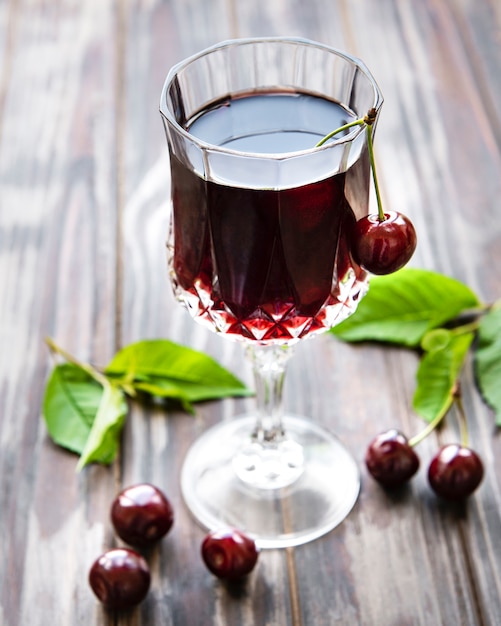 Kirschlikör in einem Glas und frischem Obst auf einem Holztisch