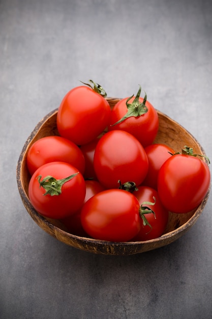 Kirschtomaten. Drei Kirschtomaten in einer Holzschale auf einem grauen Hintergrund.