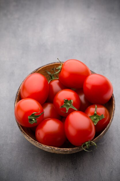 Kirschtomaten. Drei Kirschtomaten in einer Holzschale auf grau.