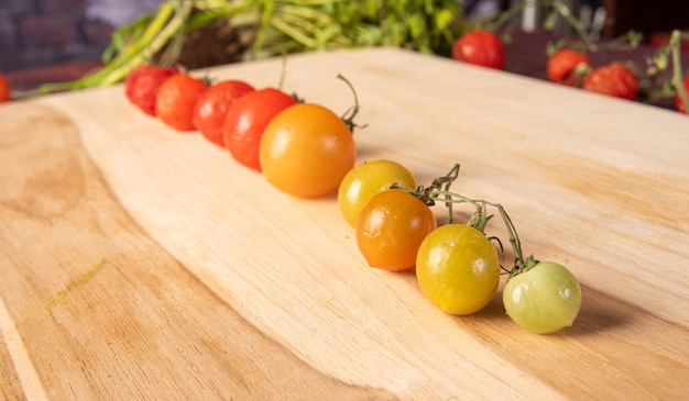 Kirschtomaten, Kirschtomaten aufgereiht von grün bis verrottend durch reif auf Holz, dunkler Hintergrund, selektiver Fokus.