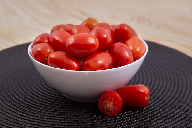 Kirschtomaten Kirschtomaten in der keramischen Schüssel auf hölzernem Hintergrund