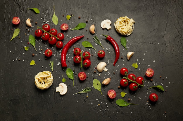 Kirschtomaten, roter Pfeffer, Knoblauch, Pilze, Nudeln, Rucola-Blätter und Gewürze auf Schwarz