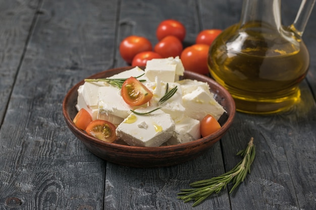 Kirschtomaten und eine Flasche Olivenöl und eine Schüssel Feta-Käse auf einem Holztisch. Salat mit Käse und Gemüse.