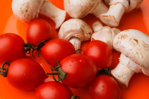 Kirschtomaten und Pilze auf orangem Hintergrund. Organisches Gemüse.