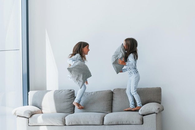 Kissenschlacht Zwei niedliche kleine Mädchen drinnen zu Hause zusammen Kinder haben Spaß