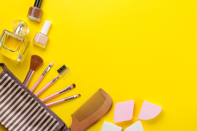 Kit de maquiagem cosméticos femininos em uma bolsa de cosméticos e pincéis de maquiagem em um fundo amarelo brilhante mulheres coisas vista superior