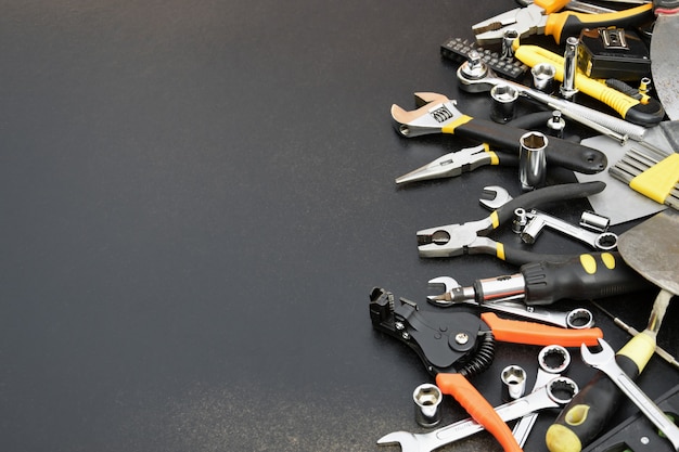 Foto kit de herramientas de manitas en mesa de madera negra. numerosas llaves y destornilladores, apiladores y otras herramientas para todo tipo de trabajos de reparación o construcción.