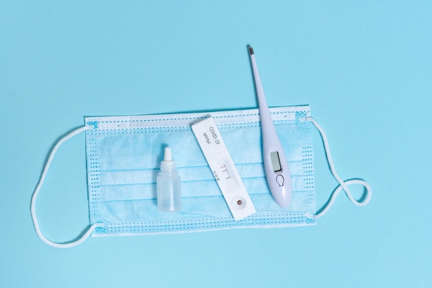 Kit higiênico para proteção contra Covid19 em um fundo azul isolado Termômetro desinfetante de máscara protetora descartável e teste de coronavírus