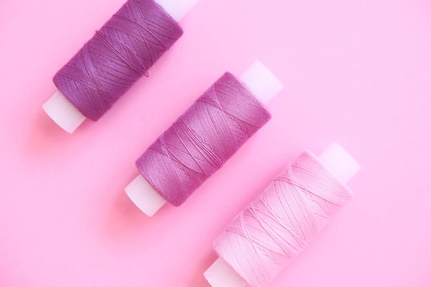 Kit de hilo de coser de hilo de coser carmesí violeta rosa lila sobre un fondo de papel rosa