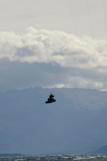 Kitesurf deportista saltando kitesurf en un lago con montañas en el fondo