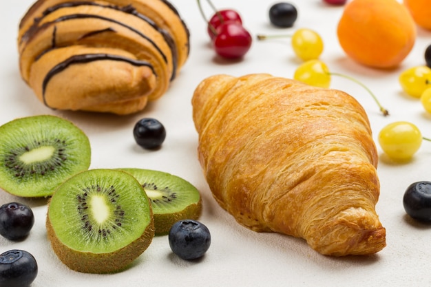 Kiwi y arándanos, croissants sobre superficie blanca. Vista superior