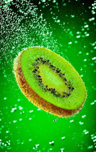 El kiwi fresco cae en el agua sobre un fondo verde