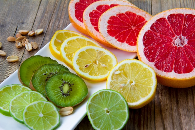 Kiwi, limón, pomelo y lima en una placa blanca sobre una mesa de madera