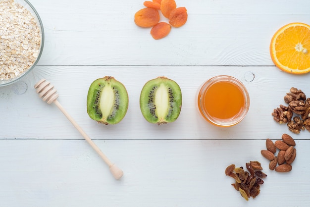 Kiwi, miel y albaricoques secos se encuentran en una mesa de madera blanca. Desayuno saludable.