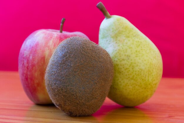 Kiwi, roter Apfel und Birne auf Holztisch. Frisches Obst auf rotem Grund. Gesundes Ernährungskonzept