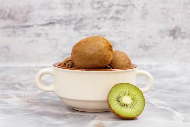 Kiwis enteros en un cuenco de porcelana sobre la mesa de piedra de la cocina. Comida sana.