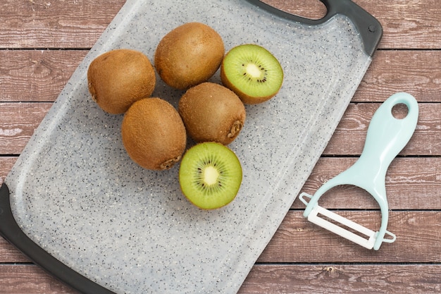 Kiwis enteros y en rodajas y un depurador sobre una tabla de cortar en el fondo de madera. Comida sana. Vista superior.