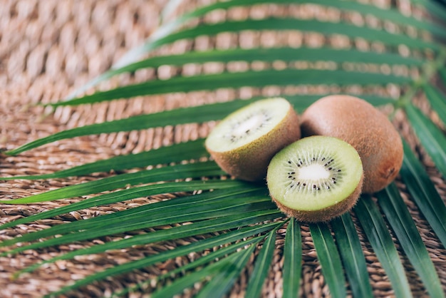 Kiwis suculentos sobre folhas de palmeira em fundo de rattan Copie o espaço Frutas exóticas de viagens tropicais Conceito vegano e vegetariano