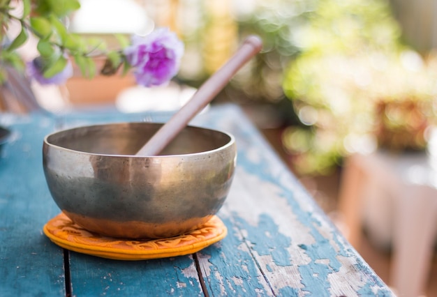 Klangschale auf einem rustikalen Holztisch mit Blumenzen im Freien