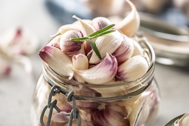 Klares Glas voller frischer aromatischer Knoblauchzehen mit Rosmarin als Dekoration.