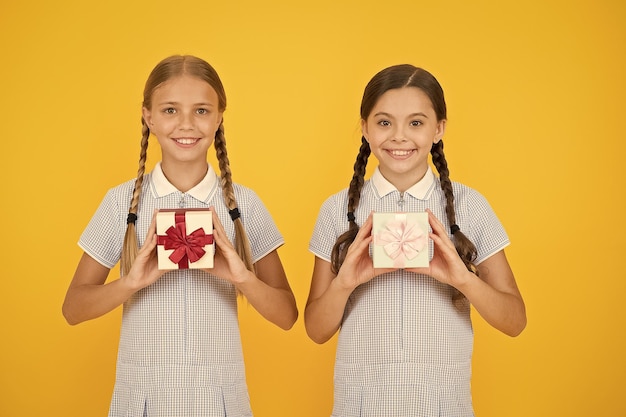 Klassenkameraden geben Geschenkboxen Bildungsprogramm für begabte Kinder Schulferien Erziehung Großzügigkeit Glück teilen Feiertagsfeier Geschenke teilen Mädchen öffnen Geschenke gelben Hintergrund