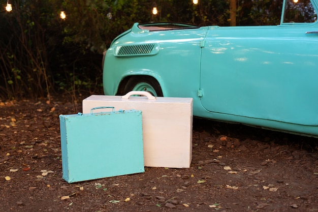 Klassische alte Vintage-Koffer mit dem Auto im Garten stehend. Ein blau-rosa Holzkoffer steht am Retro-Auto. Sommerausflug. Reisekonzept. Hochzeitsdekoration. Dekor des Hauses, Garten für den Urlaub.