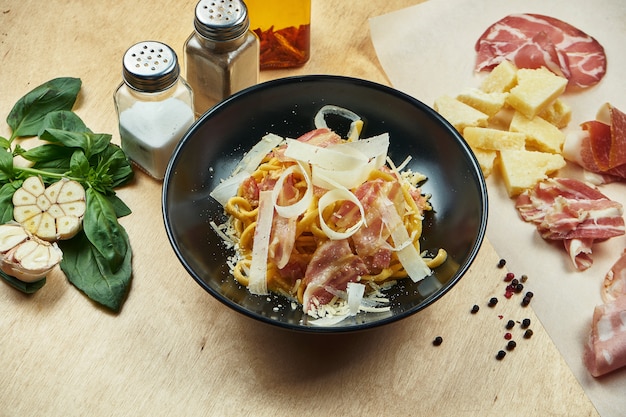 Klassische, hausgemachte Carbonara-Nudeln mit Bechamelsauce, Speck und Parmesan in schwarzer Schüssel. Traditionelle italienische Küche