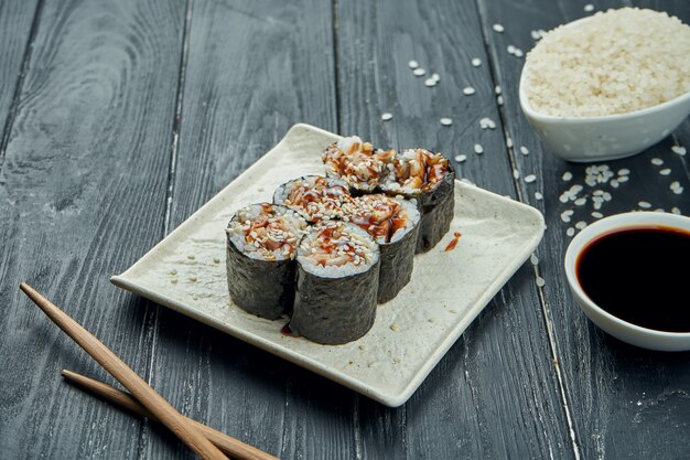 Klassische japanische Sushi-Rollen - Maki-Rollen mit Aal auf einer weißen Keramikplatte auf einem schwarzen hölzernen Hintergrund